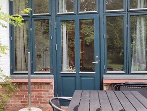 A dark blue door with glass panels, a brick wall, and a wooden table outside. - 5 Star Holiday Home in Ostermarie (Østermarie)