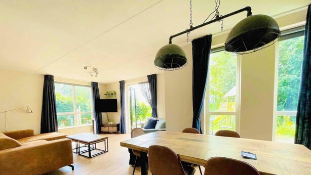 A modern living room with a wooden dining table, leather sofas, and a TV mounted on the wall. - Family Bungalow With Private Garden (Ewijk)