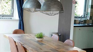 A dining area with a wooden table, four chairs, a potted plant, and pendant lights. - Family Bungalow With Private Garden (Ewijk)