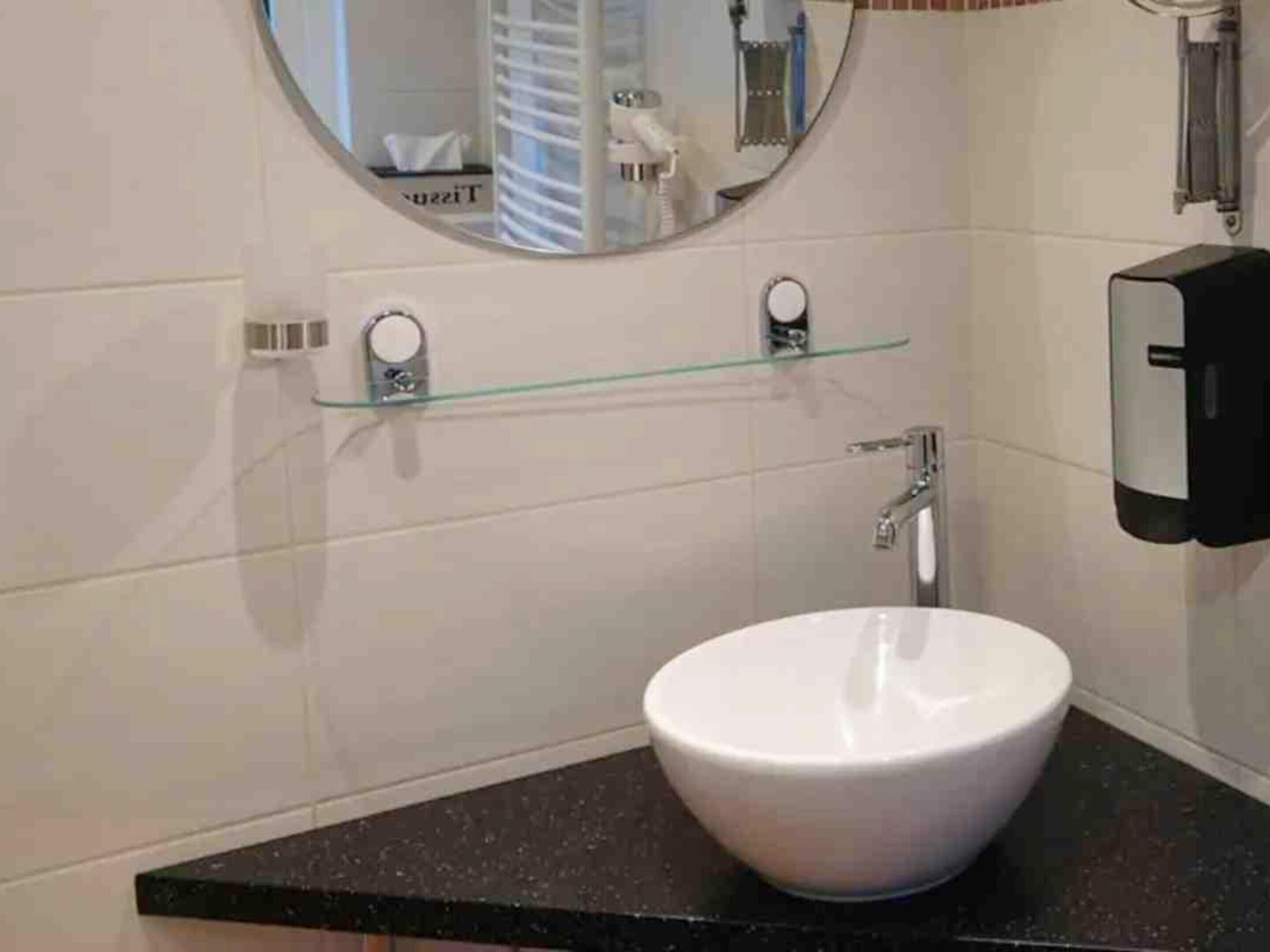 Une salle de bain avec un lavabo blanc, un miroir, un distributeur de savon et un porte-serviettes.
