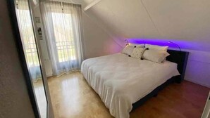 A bedroom with a bed, a window with curtains, and a ceiling with a light fixture. - Family Bungalow With Private Garden (Ewijk)