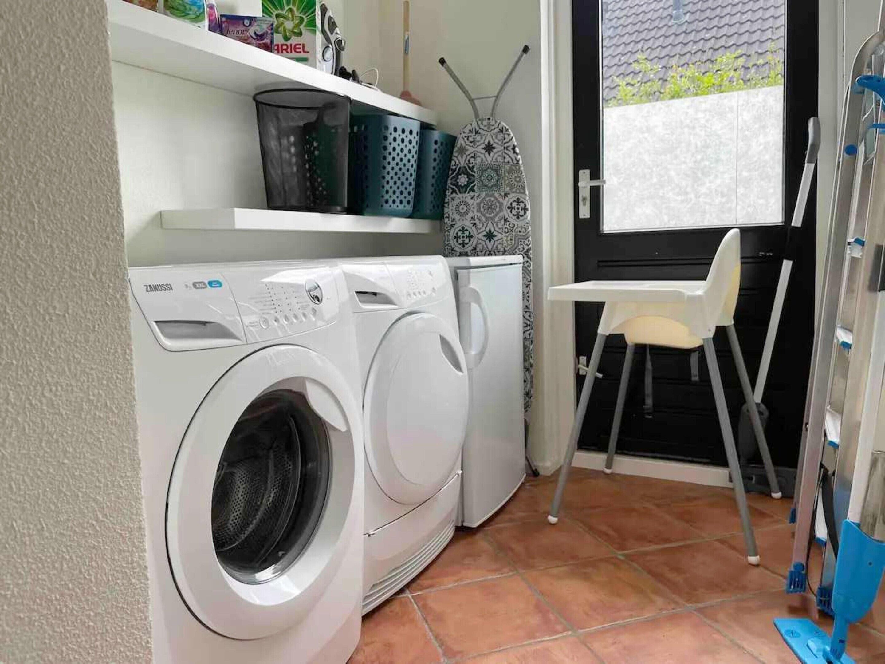 Un espace réduit dédié à la buanderie, comprenant un lave-linge, un étendoir et une chaise.