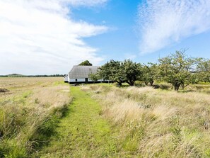 Une grange rustique, accessible par un chemin de terre, entourée de champs ouverts et d’arbres.
