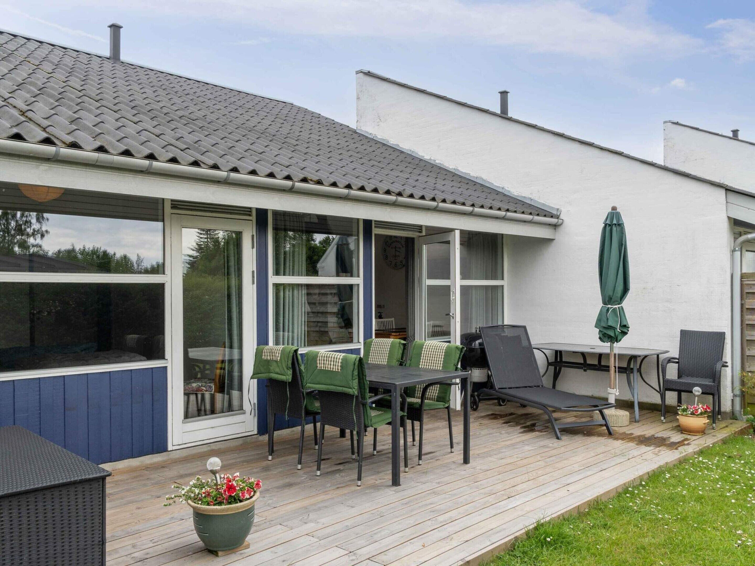 Een overdekt terras met een tafel, stoelen, een lounge fauteuil en een potplant.