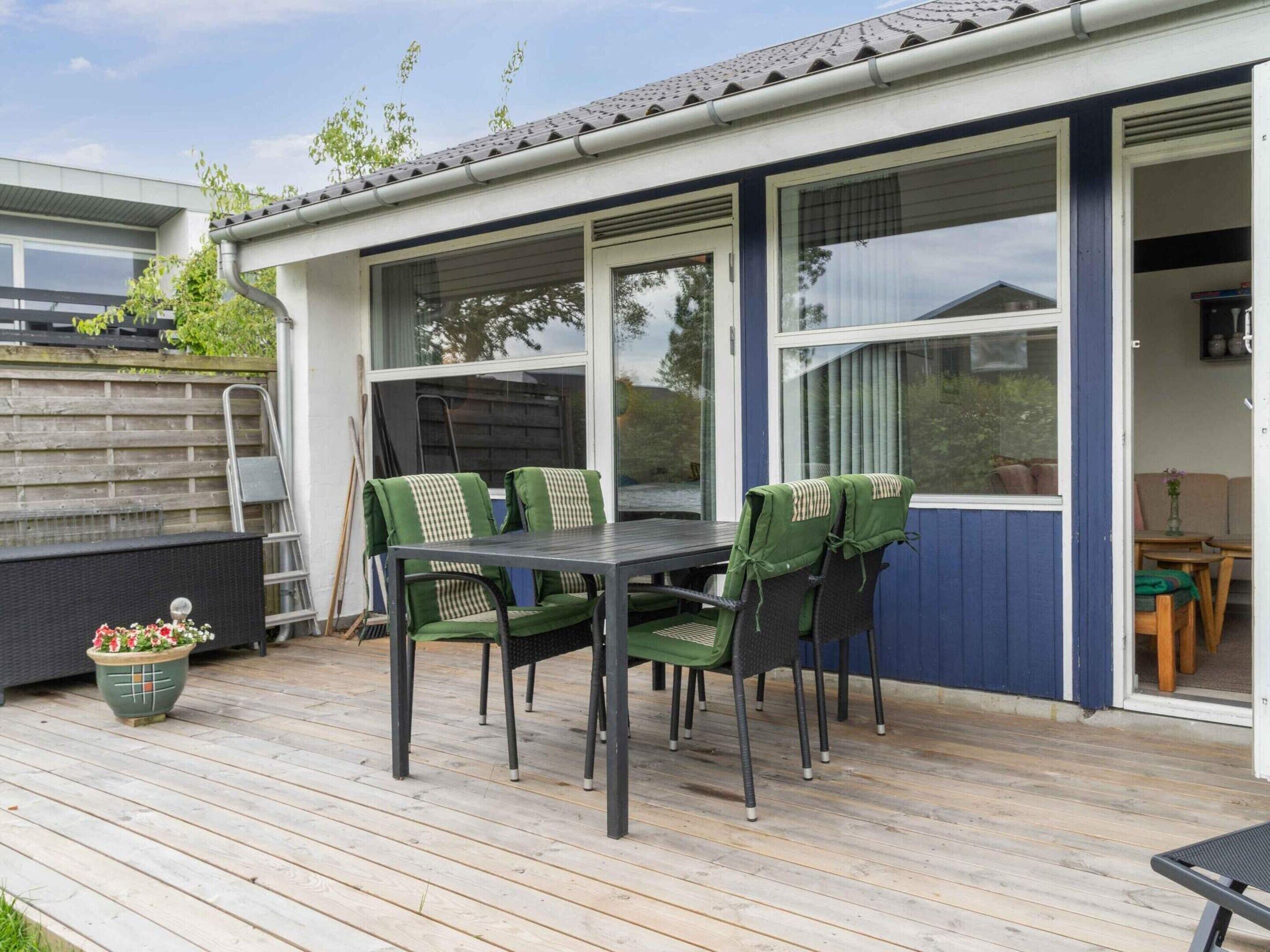 Een overdekt terras met een tafel en stoelen, een houten terras en een uitzicht op de omgeving.
