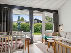 Un salón moderno con sofá, sillas, una mesita y vistas a un jardín a través de amplios ventanales.