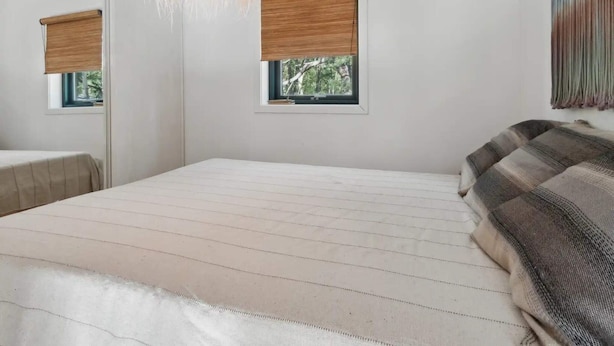 A bedroom with a bed, a hanging light fixture, two windows with blinds, and a couch.