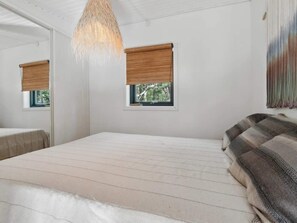 A bedroom with a bed, a hanging light fixture, two windows with blinds, and a couch.