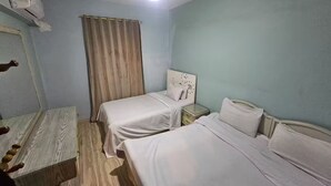 Een kamer met twee eenpersoonsbedden, een houten vloer, een plafondlamp en een raam met gordijnen.