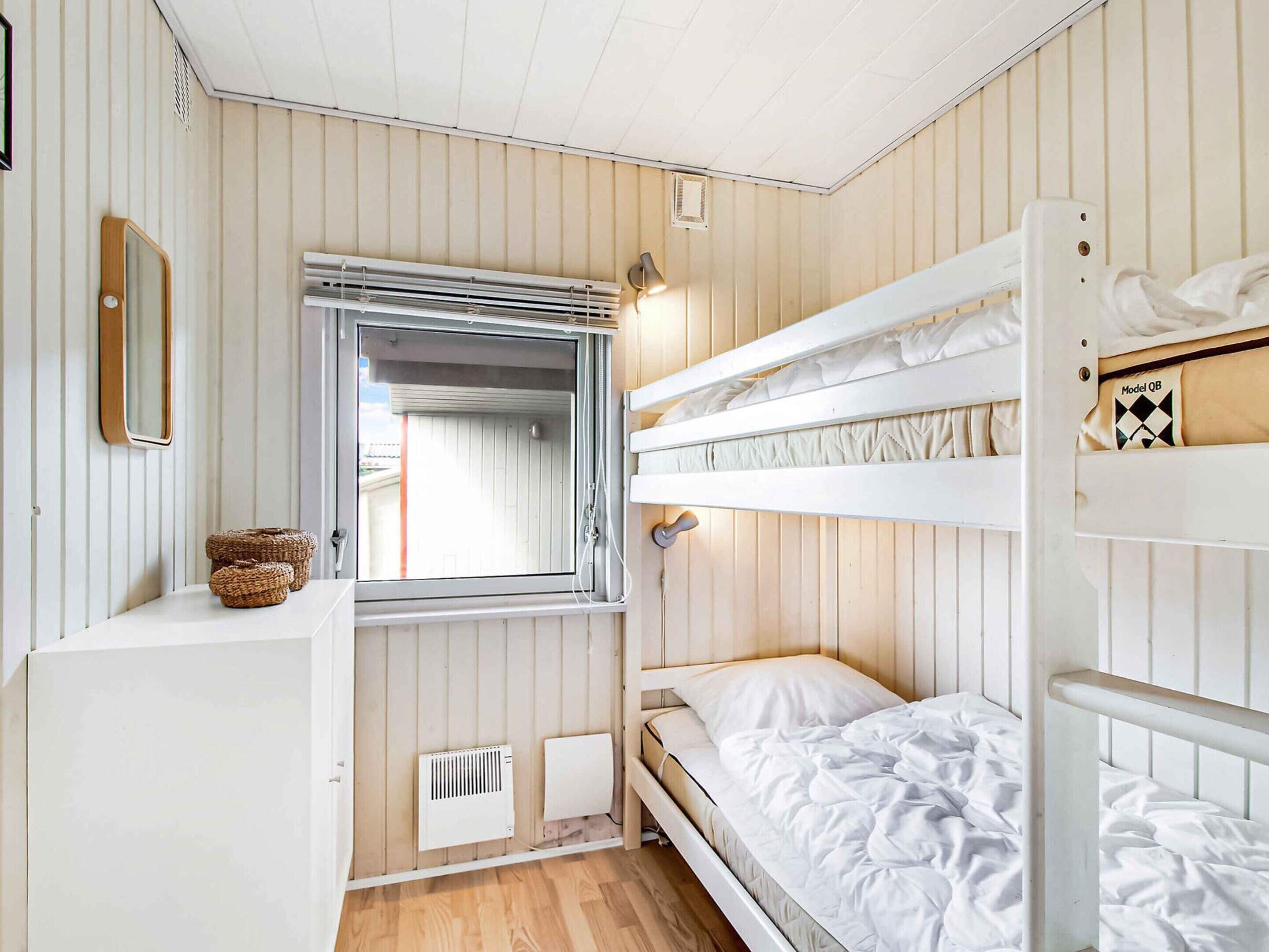 Une chambre avec un lit superposé, une fenêtre, un radiateur et une petite table avec des paniers.