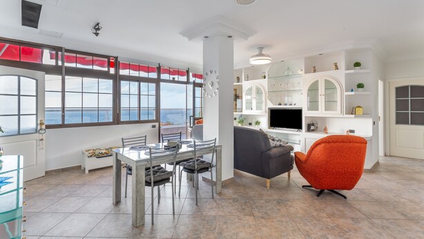 A spacious living area with a dining table, a sofa, a TV, and a view of the sea through large windows. - Vacation Home 'Crisol' with Sea View, Private Terrace and Wi-Fi (Mesa del Mar)