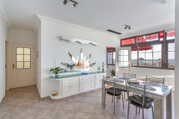 A dining area with a glass-top table, chairs, a white cabinet with drawers, and a decorative wall piece. - Vacation Home 'Crisol' with Sea View, Private Terrace and Wi-Fi (Mesa del Mar)