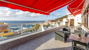 A balcony with a red awning, outdoor furniture, and a view of the sea. - Vacation Home 'Crisol' with Sea View, Private Terrace and Wi-Fi (Mesa del Mar)