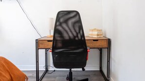 Ein Eckzimmer mit Schreibtisch aus Holz, schwarzem Bürostuhl, an der Wand befestigtem Fernseher und Holzboden.