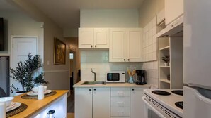 A compact kitchen with white cabinets, a microwave, a coffee maker, and a stove. - Confortable Home on Notre Dame & near Downtown (Montreal)