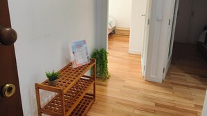 Un pasillo con suelo de madera, una puerta con pomo de latón, un pequeño estante de madera con una planta, un cuadro en la pared y una puerta abierta que da a otra habitación.