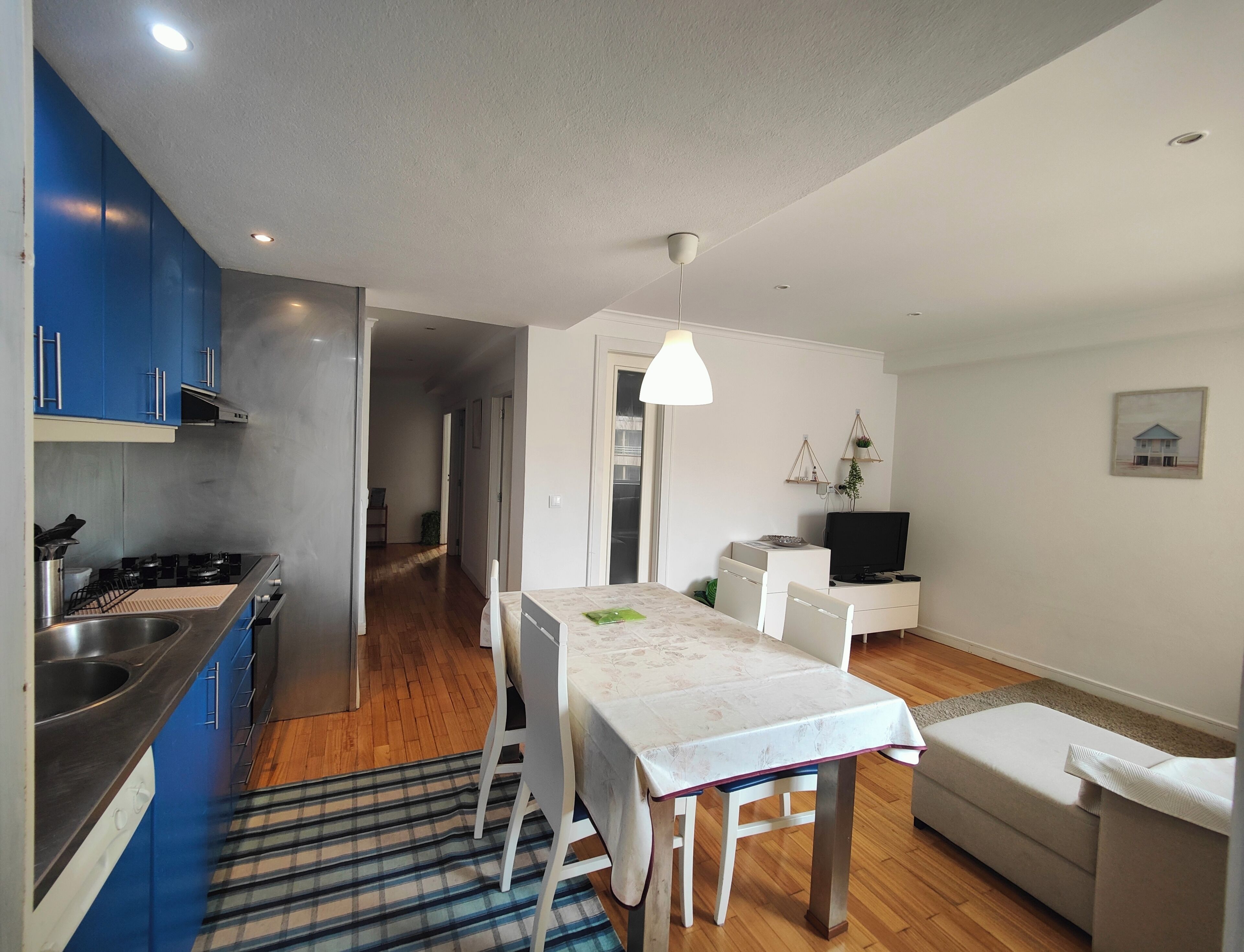 Eine moderne Küche mit blauen Schränken, ein Essbereich mit Tisch und Stühlen, eine Couch und ein Fernseher.