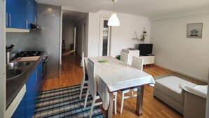 Una cocina moderna con armarios azules, una zona de comedor con mesa y sillas, un sofá y un televisor.