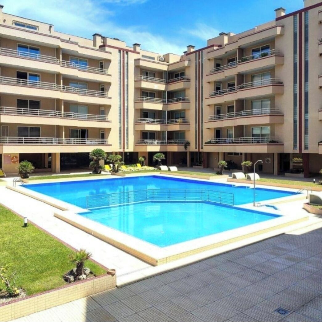 Ein mehrstöckiges Hotel mit einem zentral gelegenen Schwimmbecken, umgeben von einer gefliesten Terrasse.