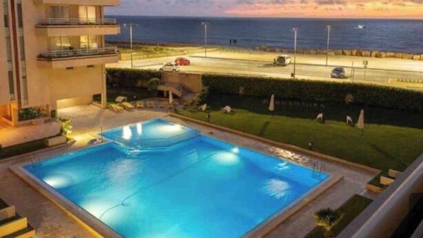 Un hotel moderno con piscina, vistas al mar y una carretera al fondo.