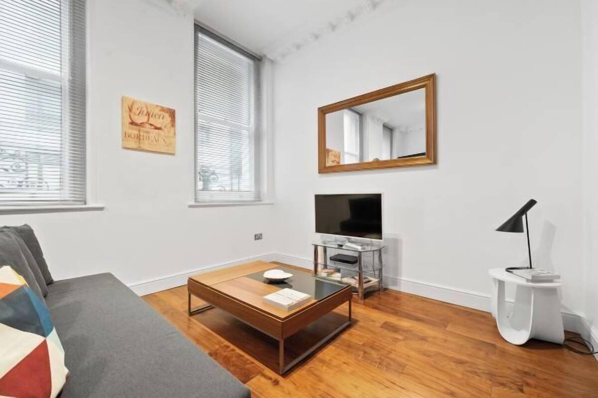 A modern living room with a sofa, a coffee table, a TV on a stand, and a mirror on the wall.