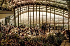 A spacious atrium with a high ceiling, large windows, and abundant indoor plants. - Apartment 2, 48 Bishopsgate by City Living London (London)