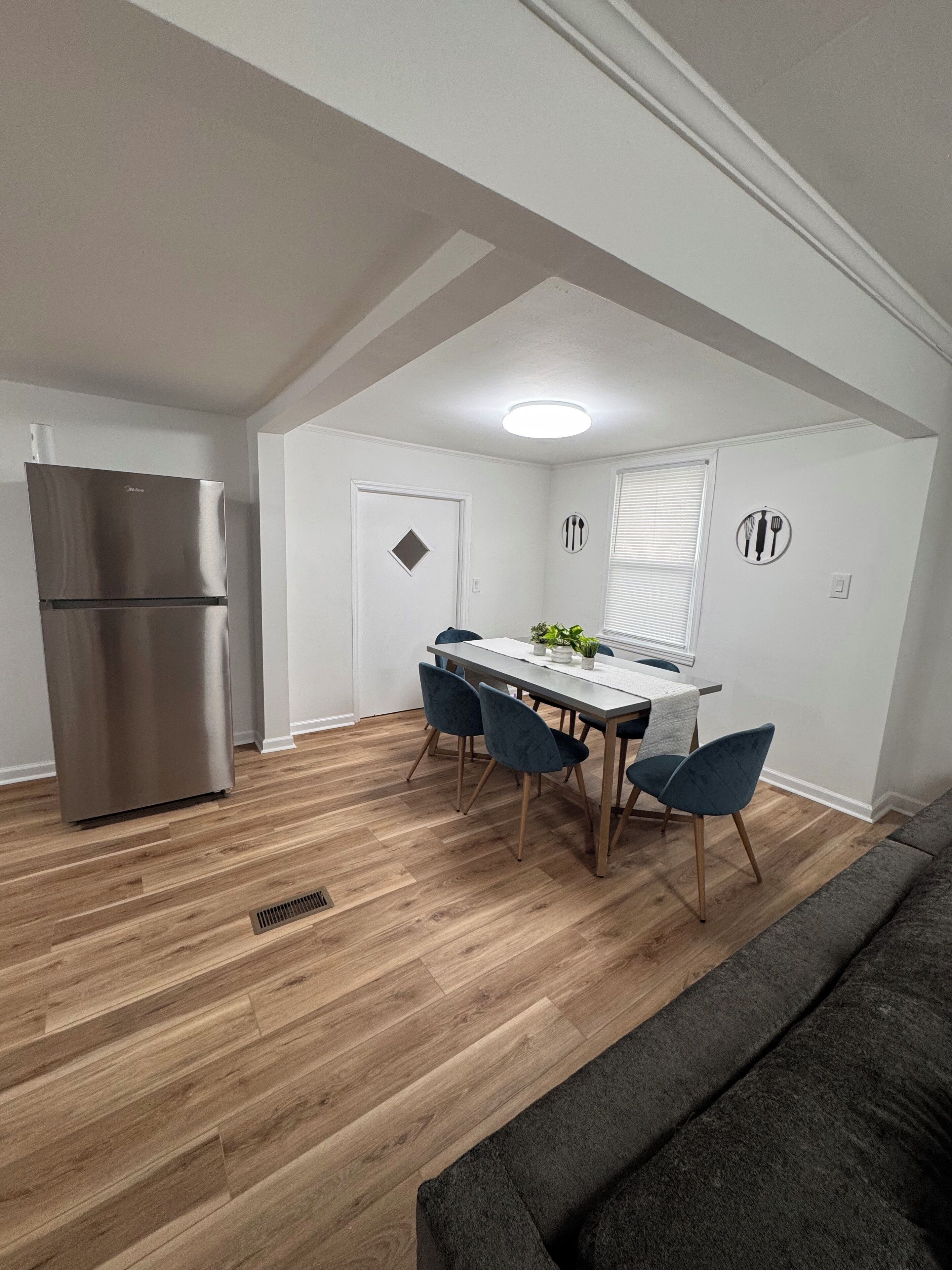 Una cocina moderna con un refrigerador de acero inoxidable, una mesa de comedor con sillas y un sofá gris.