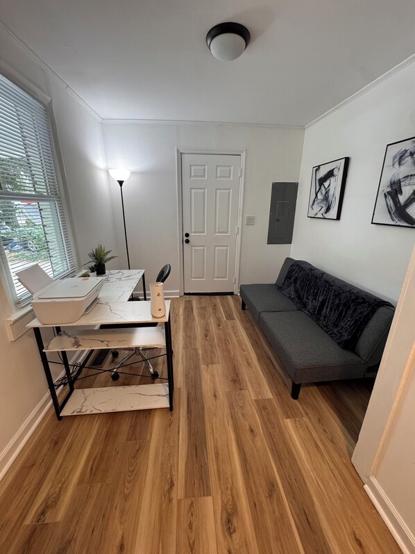 Una habitación con escritorio, silla, sofá, lámpara y una puerta.