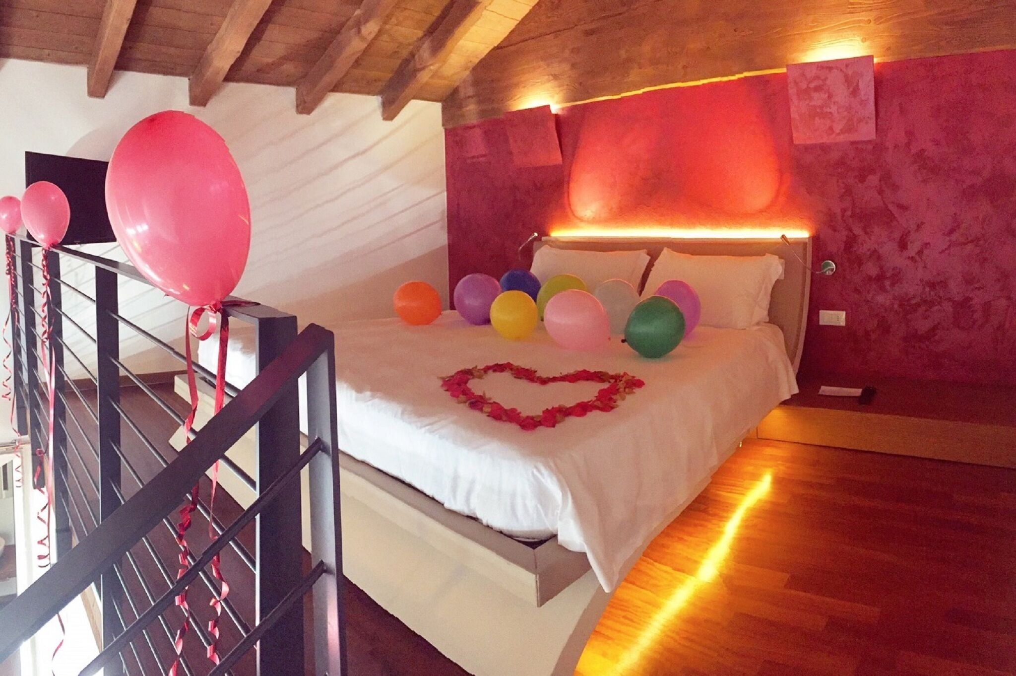 Ein Schlafzimmer mit einem Bett, Luftballons und einer herzförmigen Dekoration auf dem Bett.