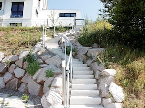 A stone staircase leading up to a building with a metal railing, surrounded by rocks and vegetation.