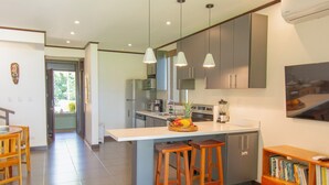 Une cuisine moderne avec un îlot central, des tabourets en bois et une bibliothèque.