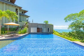 Una piscina con vistas al océano, un porche cubierto con mesa y sillas, y un edificio pequeño con balcón.