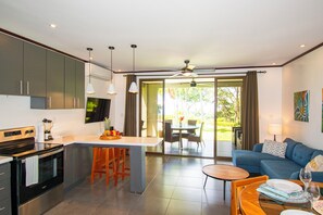 Una cocina moderna con una isla central, un comedor con mesa y sillas, y una sala de estar con sofá y ventilador de techo.