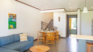 Un salon avec un canapé bleu, une table ronde en bois et un coin repas comprenant des chaises en bois et une table dressée pour quatre personnes.