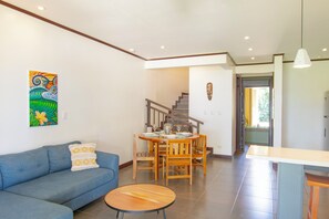 Una sala de estar con un sofá azul, una mesa redonda de madera y un comedor con sillas de madera y una mesa dispuesta para cuatro.