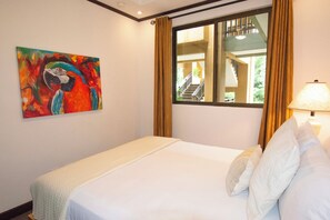 Een hotelkamer met een bed, een schilderij aan de muur, een raam met gordijnen en een lamp.