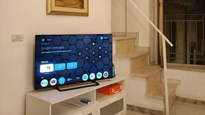 Ein Wohnzimmer mit einem Flachbildfernseher auf einer weißen Unterhaltungseinheit, einem gerahmten Bild an der Wand und einer Treppe, die zu einem Balkon führt.
