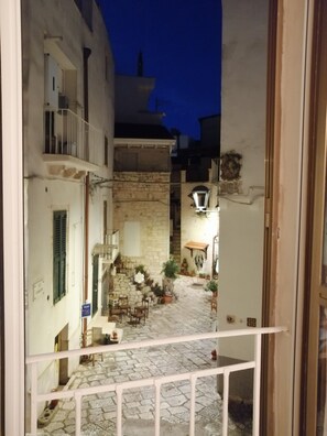 Un estrecho callejón con paredes de piedra, un pequeño patio con algunas macetas y una escalera que sube a un nivel superior.