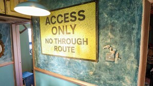 Un panneau indiquant « ACCÈS AUTORISÉ, PAS DE TRAVERSÉE » est fixé à un mur dont la surface est bleue et verte et présente une texture particulière.