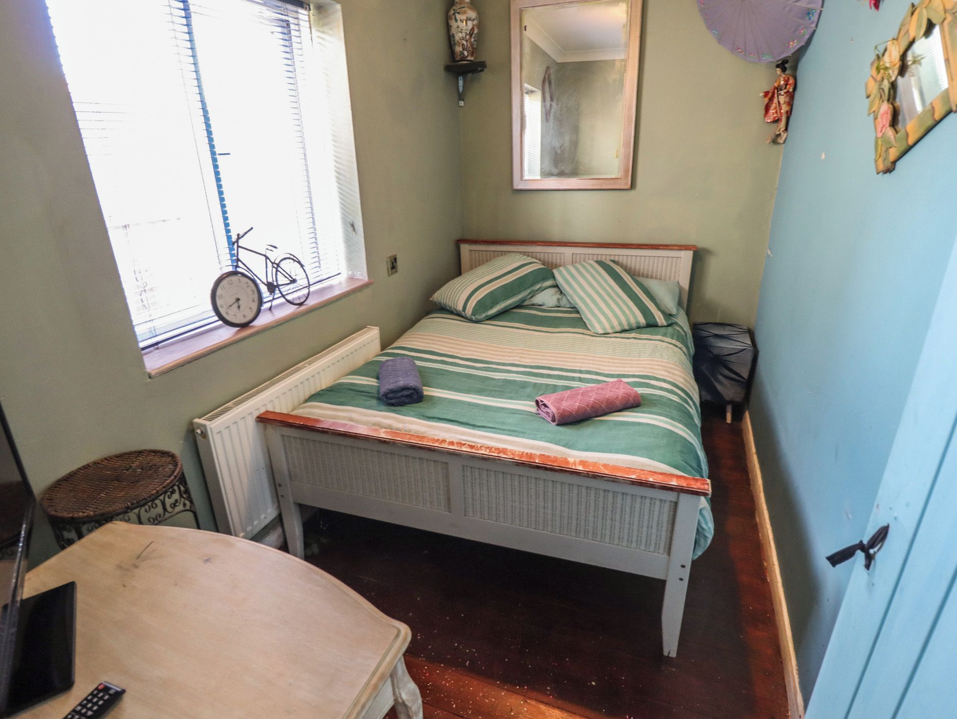 Un dormitorio pequeño con una cama individual, una ventana con una bicicleta, un radiador, un espejo y una puerta.