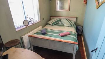 Un dormitorio pequeño con una cama individual, una ventana con una bicicleta, un radiador, un espejo y una puerta.
