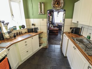 A kitchen with white cabinets, a black countertop, and a stove. - Dormy Cottage (Skegness)