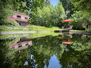 A house with a red roof, a pond, and a red umbrella. - Holiday Home 'Alpenblick' with Mountain View, Private Terrace and Wi-Fi (Rickenbach)