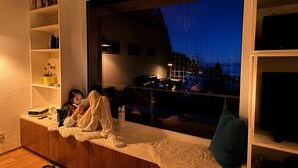 A cozy living room with a large window, wooden flooring, and bookshelves. - Holiday Home 'Alpenblick' with Mountain View, Private Terrace and Wi-Fi (Rickenbach)