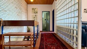 Un couloir avec un plafond en bois, un tapis à motifs, un banc et un mur en blocs de verre.