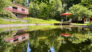 A house with a balcony, a pond with a red boat, and a red umbrella. - Holiday Home 'Alpenblick' with Mountain View, Private Terrace and Wi-Fi (Rickenbach)