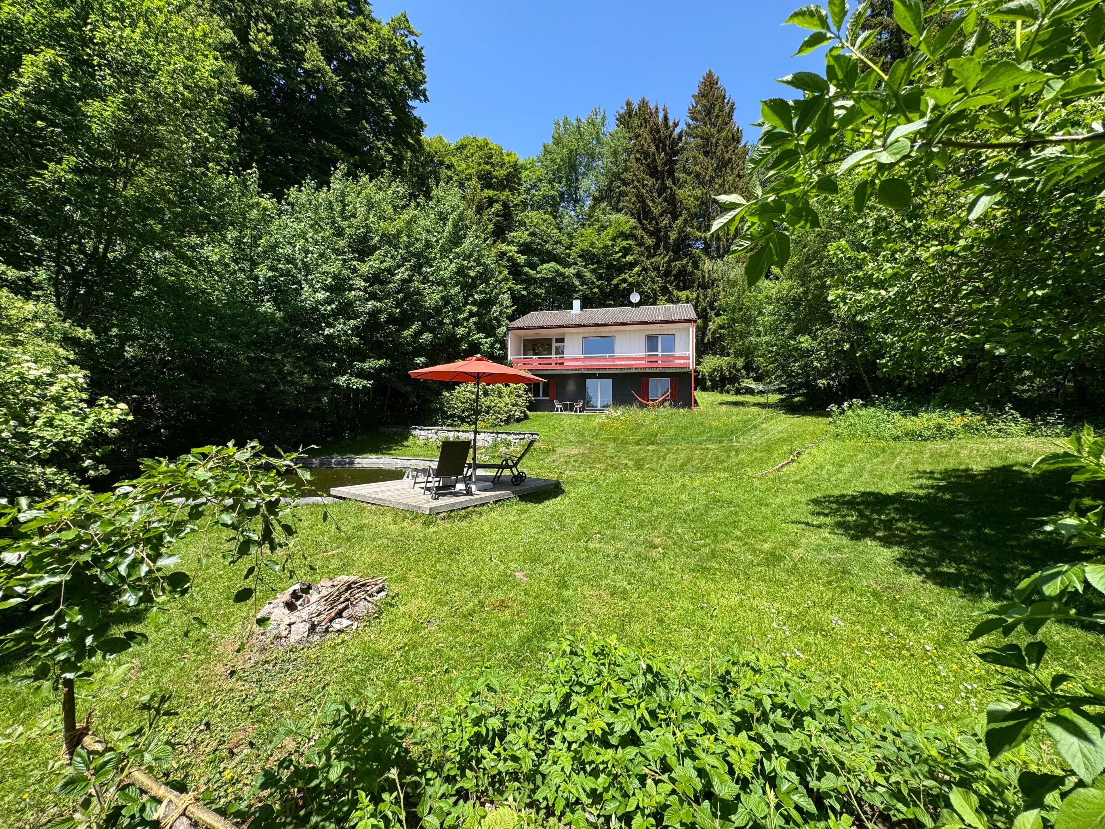 Une maison avec une terrasse, une petite piscine et un parasol rouge.