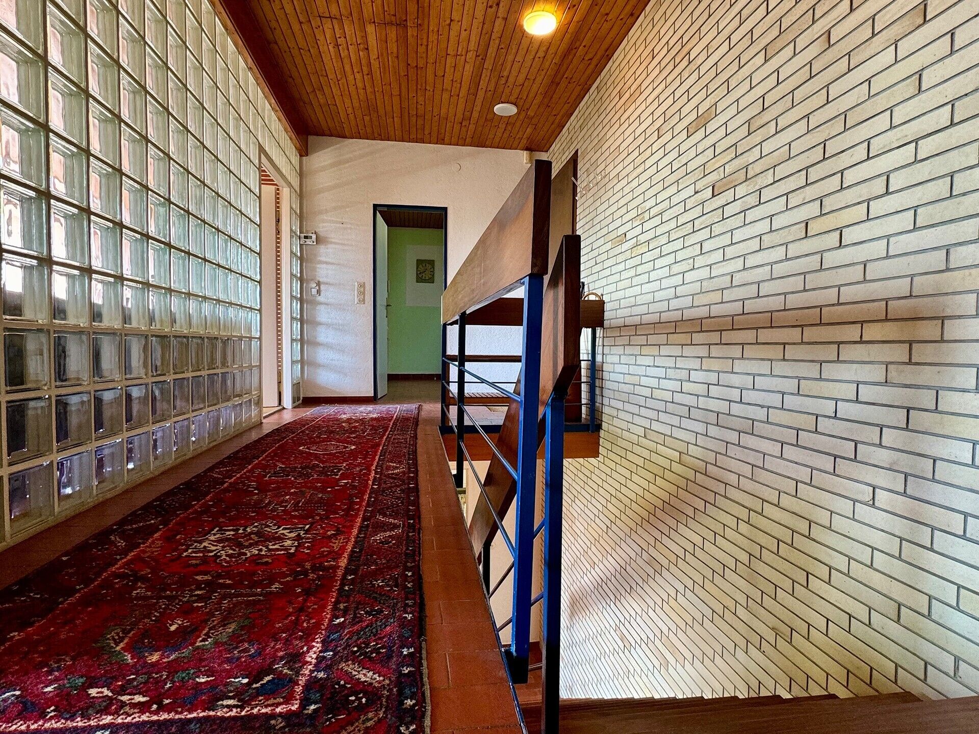 Un couloir avec un tapis rouge à motifs, un plafond en bois et des murs en briques.