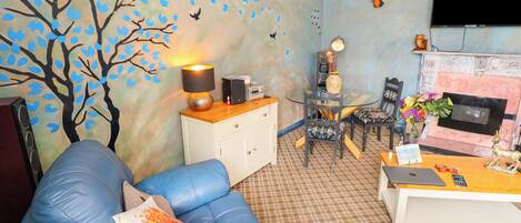 Una sala de estar con un sofá azul, un sofá rojo, una mesa de centro, una chimenea y una pared con un mural de un árbol.