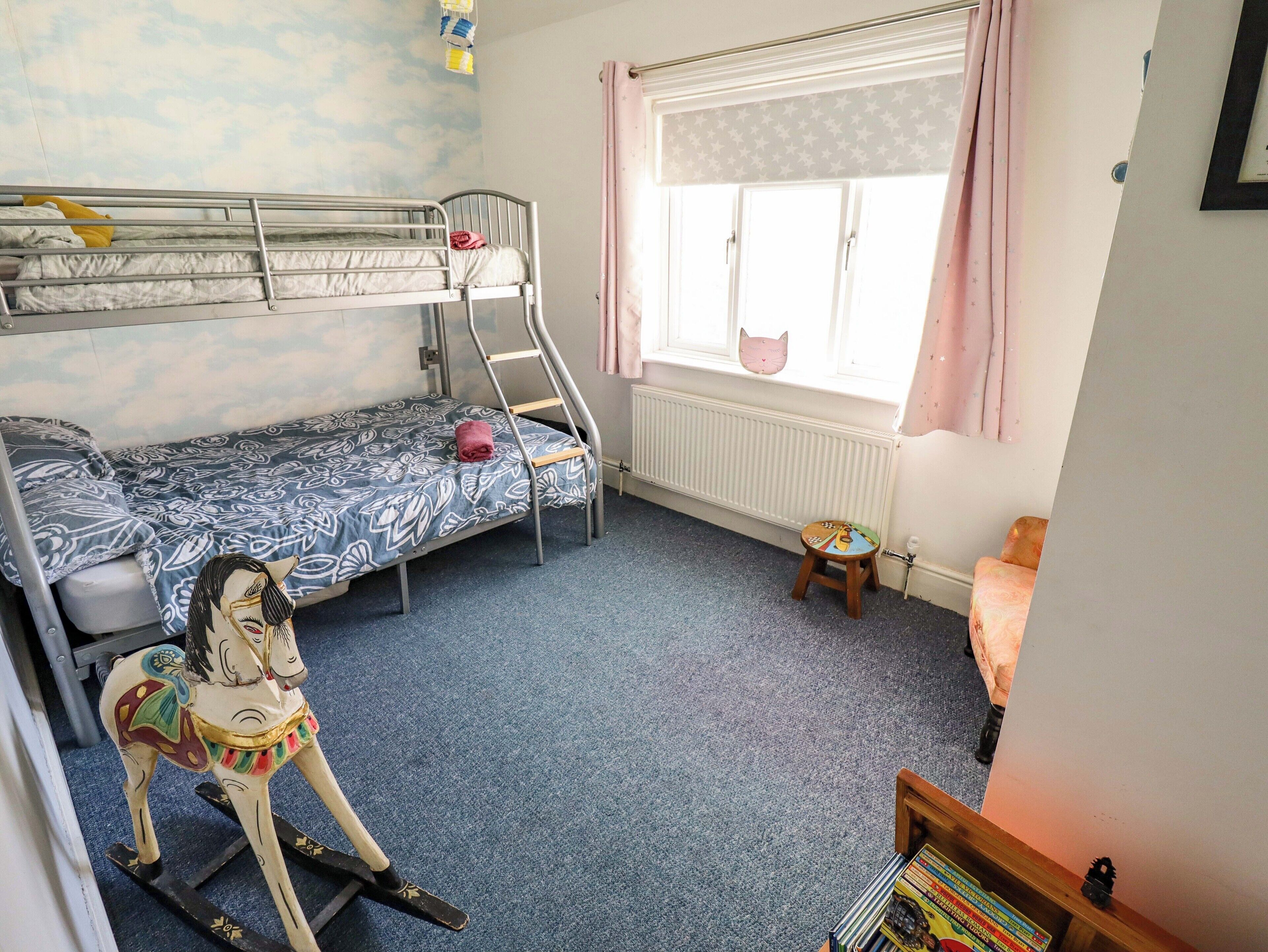 A child's bedroom with bunk beds, a rocking horse, a window with curtains, and a radiator.